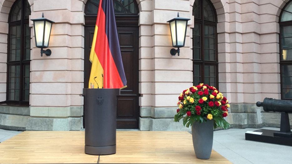 Rednerpult mit Deutschlandflagge und Blumenvase