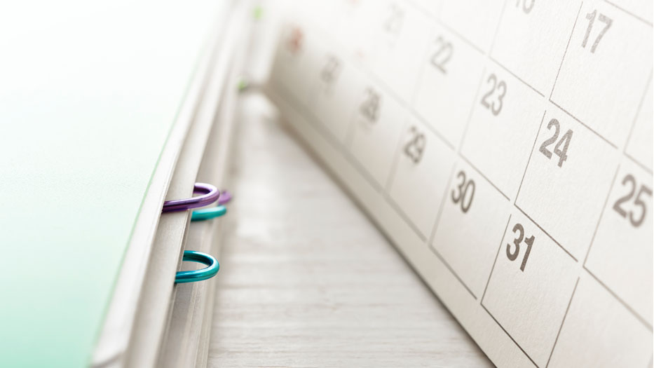 Assorted files, some fastened with paperclips, are visible under a mint-coloured file folder. On the right is a small table-top calendar turned to a month with 31 days.