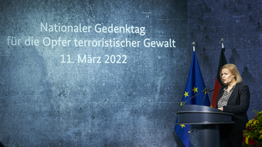Bundesinnenministerin Nancy Faeser am Rednerpult. Neben Ihr steht in weißen Buchstaben auf einem blaumellierten Hintergrund "Nationaler Gedenktag für die Opfer terroristischer Gewalt 11. März 2022" (Aufnahme von der Seite)