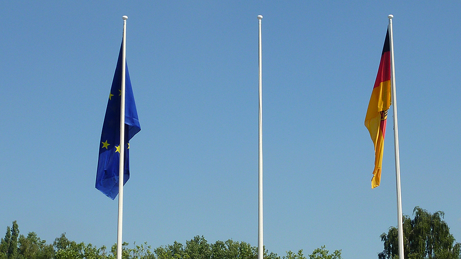 Europaflagge links und Bundesdienstflagge rechts von einem unbeflaggten Mast